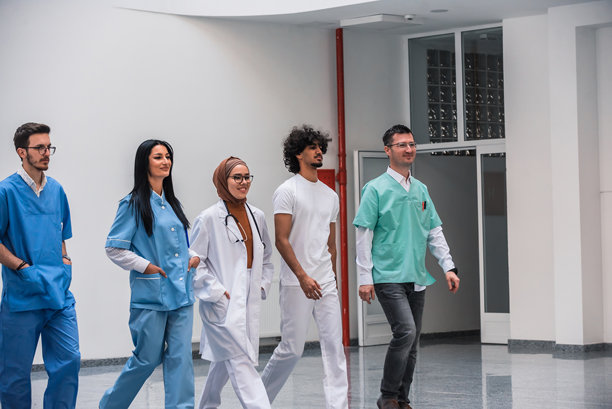 一群不同背景的医护人员（医生、护士）在医院走廊里并肩行走。该图片适合用于医疗健康和医学概念相关主题。图片下载