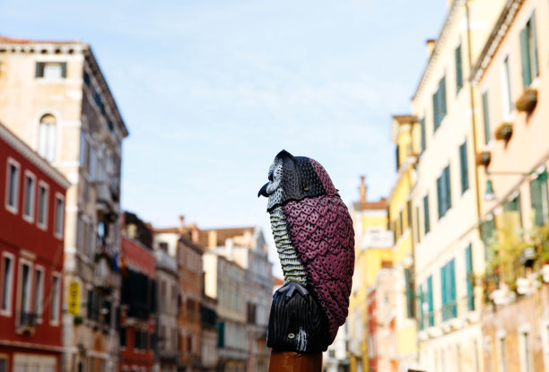 色彩鲜艳的猫头鹰雕塑，坐落在风景如画的威尼斯街道上的柱子上，背景展示着充满活力的建筑和迷人的运河图片下载