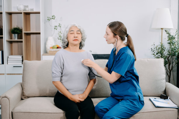 年轻的护士在房间里搀扶着一位老人行走，握着她的手给予支持。这是在辅助生活设施中，伤后治疗和康复的场景。图片下载