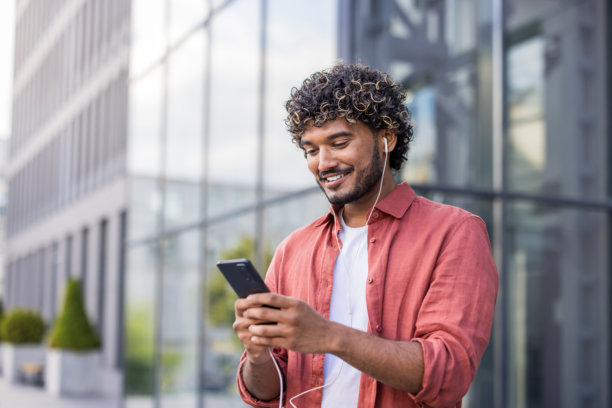 一名年轻的印度男子戴着耳机在户外使用手机的特写照片图片下载