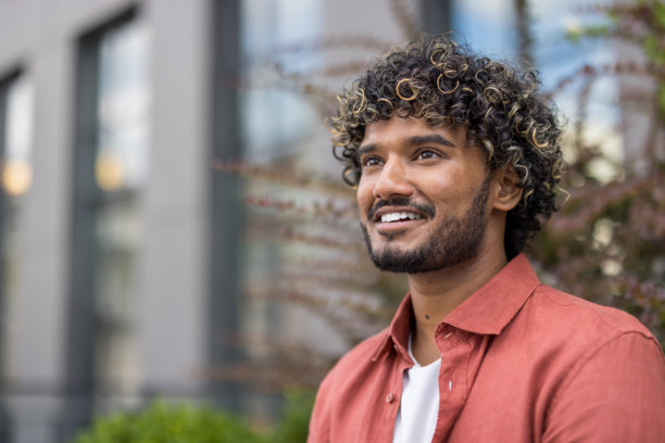 一名穿着红色衬衫的年轻印度男子坐在户外，侧身微笑的特写照片图片下载