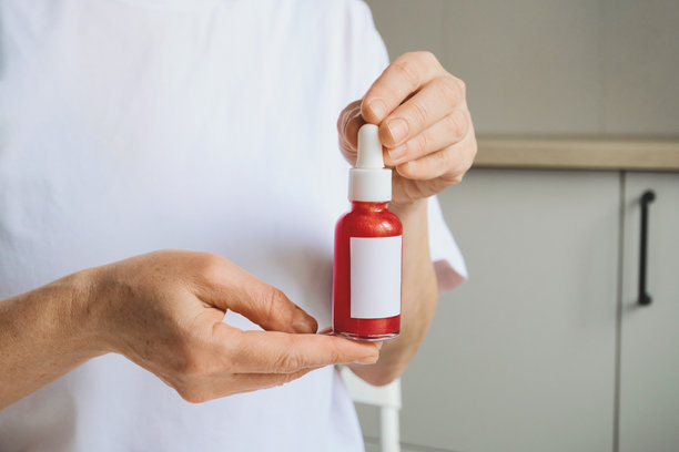 女性双手持有一个无标记的红色滴管瓶，用于护肤精华液图片下载