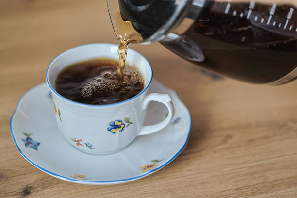 木桌上，一壶红茶倒入带有花卉图案的杯中，素材图片图片下载