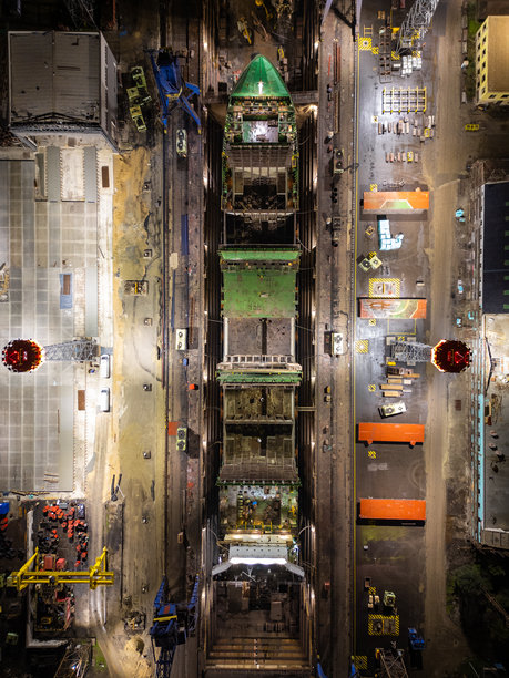 工业船厂干船坞内大型船舶维修的夜间航拍照片，俯视角度展示了船坞基础设施、起重机、平台和灯火通明的维修区域图片下载