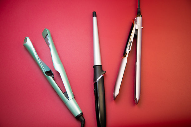 粉色背景中央摆放着用于拉直和卷曲头发的造型器和卷发棒。体现了头发护理、发型设计、美发的概念。图片下载