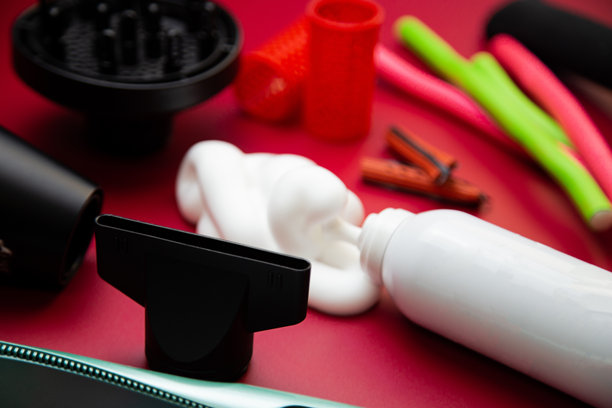 粉色背景下的吹风机特写侧视图，配有直发和卷发造型的各种附件、造型器和卷发棒，以及用于增加丰盈度和持久度的发泡产品，还有各种形状和尺寸的卷发器。展示了头发护理、发型设计和美发的概念。图片下载