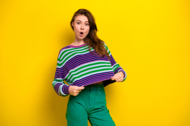 条纹毛衣的年轻女子摆出惊讶的表情，背景是明亮的黄色，适用于生活方式时尚和广告图库照片图片下载