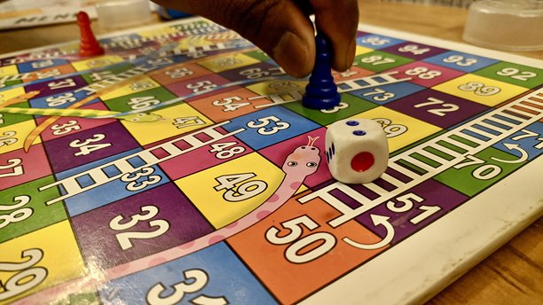 一张色彩鲜艳的蛇梯棋盘游戏的特写照片，棋盘上放有骰子和玩家棋子，代表着传统的室内游戏、家庭娱乐、儿童玩耍和教育活动。图片下载