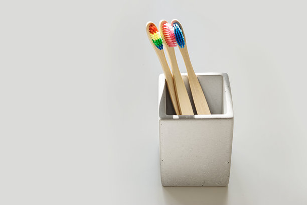 阳光下，窗户投下的阴影映照着方形灰色水泥牙刷架上的彩色竹制环保牙刷。可持续生活理念，极简风格美学照片图片下载