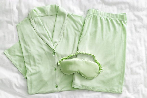 俯视白色床上的淡绿色女士睡衣，配有缎面眼罩。极简平铺风格，舒适的居家睡衣，适合睡眠和放松。美学生活方式风格的时尚睡衣照片。图片下载