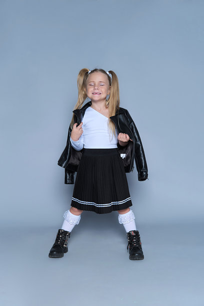 一位自信的年轻女孩肖像照，她身着现代服饰，包括皮夹克、黑色靴子和百褶裙。她大胆的姿态和俏皮的表情，使其成为儿童时尚、生活方式或肖像摄影的完美素材。图片下载