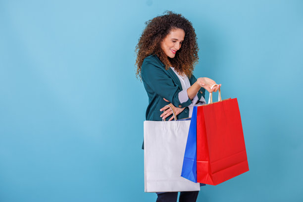 快乐的卷发女子正在查看购物袋，享受购物带来的愉悦和促销优惠图片下载
