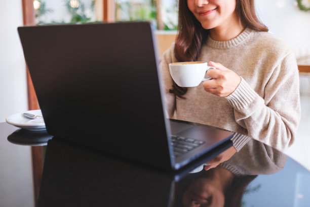 咖啡馆里，一位女士正在用笔记本电脑工作，同时喝着咖啡的特写照片图片下载