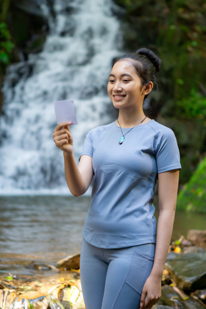 亚洲女子独自旅行，手持瀑布背景的照片纸。图片下载
