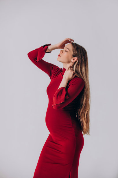 年轻美丽的孕妇模特，留着长发，身穿漂亮的红色连衣裙，在摄影棚内图片下载