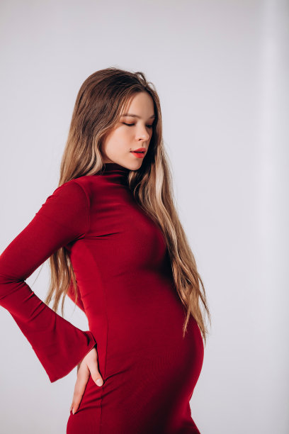 年轻美丽的孕妇模特，留着长发，身穿漂亮的红色连衣裙，在影棚里图片下载