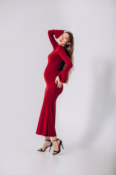 年轻漂亮的模特孕妇，留着长发，身穿漂亮的红色连衣裙，在影棚内图片下载