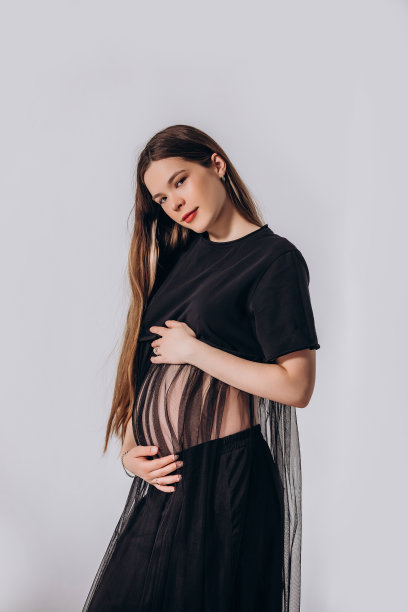 年轻漂亮的孕妇模特，留着长发，身穿漂亮的黑色连衣裙，在影棚内图片下载