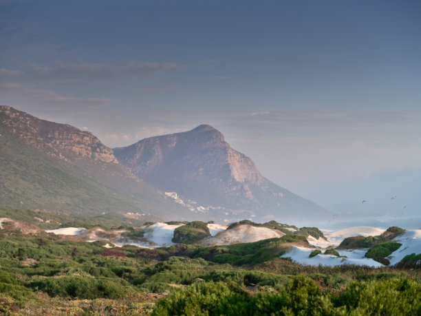 南非西开普省开普敦附近的戏剧性海岸沙丘和山地景观，有蓝天、远处的村庄和宁静的海景图片下载