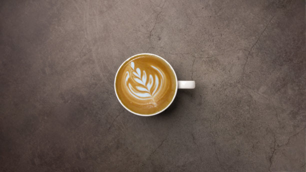 深色粗糙混凝土石桌背景下的白色杯子里的拿铁咖啡拉花，俯视角度。图片下载