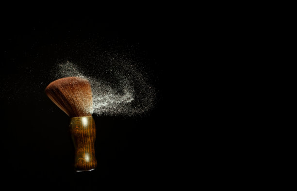 大号柔软化妆刷，伴随粉末飞溅。化妆刷飞溅出带有银色闪光的粉尘，用于化妆。黑色背景，独立照片元素图片下载
