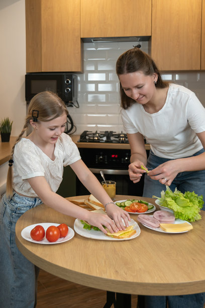 两个姐妹在家里的厨房里，用新鲜食材制作三明治，交流分享烹饪经验，一起制作健康餐食。竖版照片图片下载