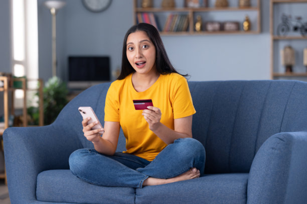 身穿现代服装的美丽年轻女子在家中沙发上喝咖啡，进行在线购物的素材照片图片下载