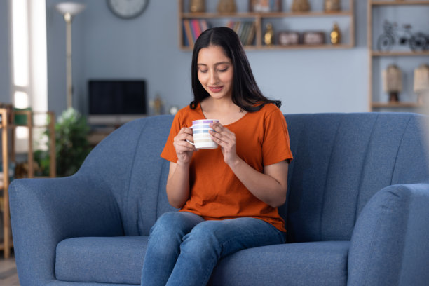 身穿现代服装的年轻美丽女孩在沙发上喝咖啡的居家照片图片下载