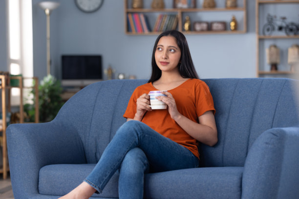 穿着现代服装的美丽年轻女子在家中坐在沙发上喝咖啡的图片图片下载