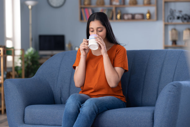 照片：一位穿着时尚的年轻漂亮女孩在家坐在沙发上喝咖啡图片下载