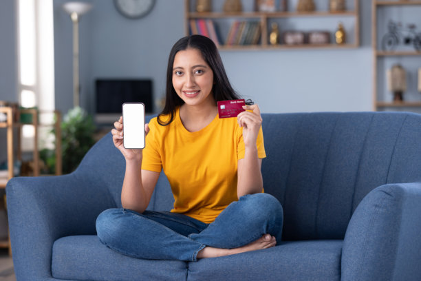身穿现代服装的美丽年轻女子在家中沙发上喝咖啡，进行在线购物的实拍照片图片下载