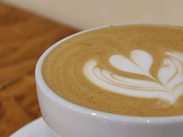 特写镜头下，一杯咖啡的细腻拉花，上面是精致的心形图案。温暖的咖啡色调与白色奶泡形成鲜明对比，营造出诱人的氛围。图片下载