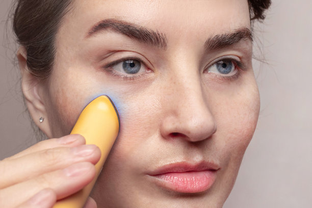 特写照片，一位白种女人在家中使用微电流面部紧致仪。流行的LED美容仪，用于眼部护理。图片下载