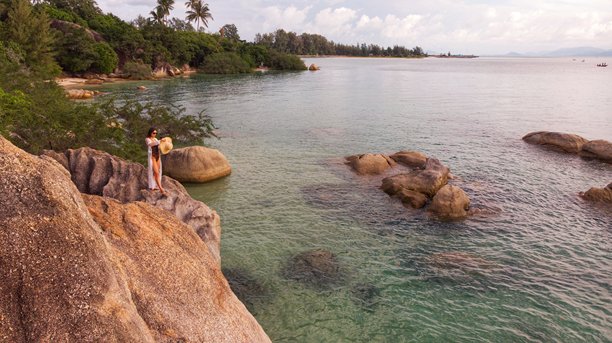身着头纱和太阳帽的年轻女孩在泰国苏梅岛的热带岩石海岸摆姿势，航拍照片图片下载