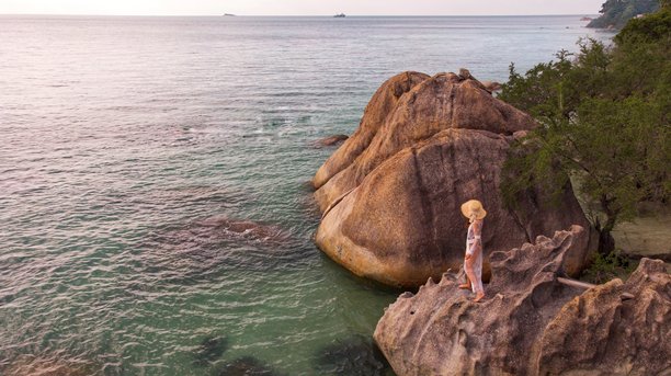 身着头巾和太阳帽的年轻女孩在泰国苏梅岛的热带岩石海岸摆姿势，航拍照片图片下载