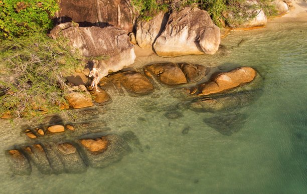 泰国苏梅岛热带岩石海岸上戴着面纱和太阳帽摆姿势的年轻女孩，航拍照片图片下载