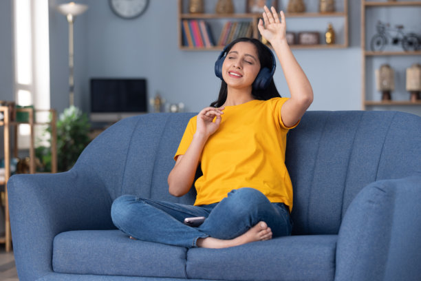 身穿黄色T恤的可爱年轻女孩在家坐在沙发上听音乐的真实照片图片下载
