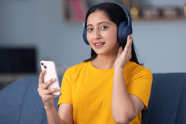 照片：一个穿着黄色T恤的可爱年轻女孩，在家坐在沙发上听音乐的素材照片图片下载