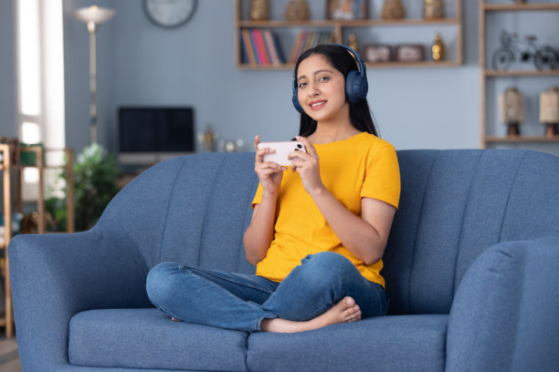 身穿黄色T恤的可爱小女孩在家中沙发上听音乐的图片素材图片下载