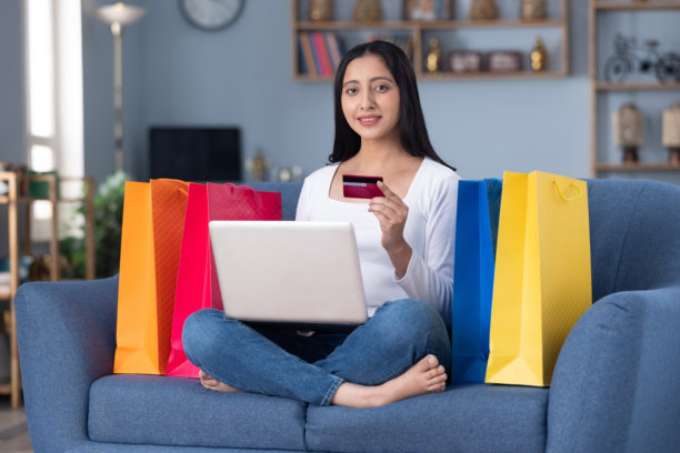 漂亮的年轻女孩在家里的沙发上用笔记本电脑在线购物的图片图片下载