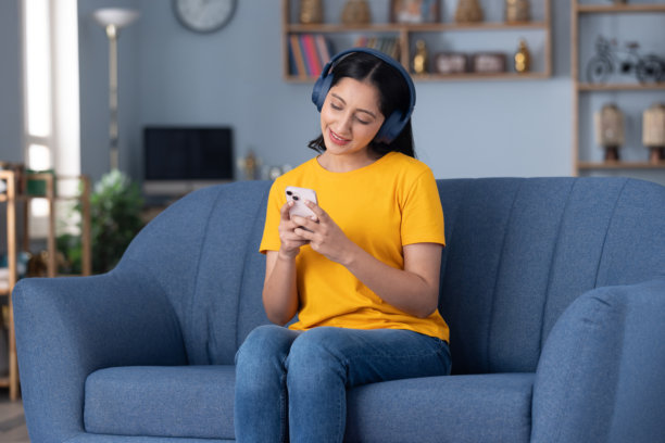 身穿黄色T恤的可爱年轻女孩在家中沙发上听音乐的库存照片图片下载