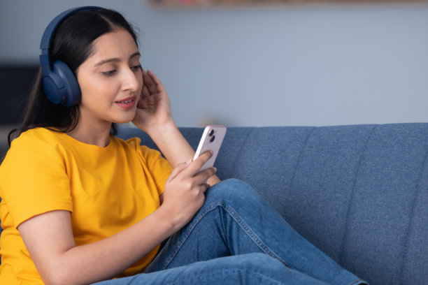 身穿黄色T恤的可爱年轻女孩在家中沙发上听音乐的库存照片图片下载
