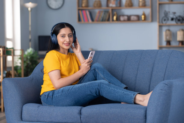 可爱的小女孩穿着黄色T恤，在家里的沙发上听音乐的居家照片图片下载