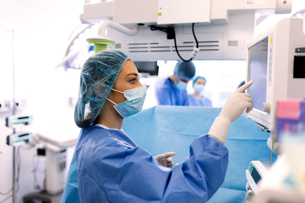 身穿蓝色手术服的麻醉师在手术室的医疗屏幕上监测病人的生命体征。专家在手术过程中调整麻醉机设置。图片下载