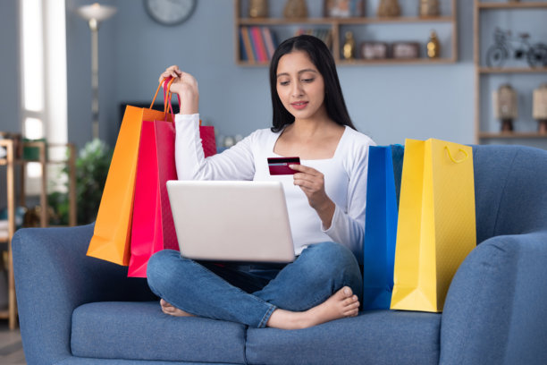 美丽的年轻女孩在家里的沙发上坐在笔记本电脑前进行在线购物的图片图片下载