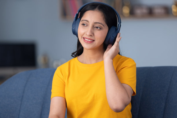 照片：可爱的小女孩穿着黄色T恤，在家坐在沙发上听音乐图片下载