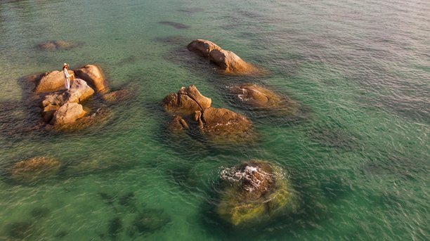 泰国苏梅岛热带岩石海岸上戴着面纱和太阳帽摆姿势的年轻女孩，航拍照片图片下载