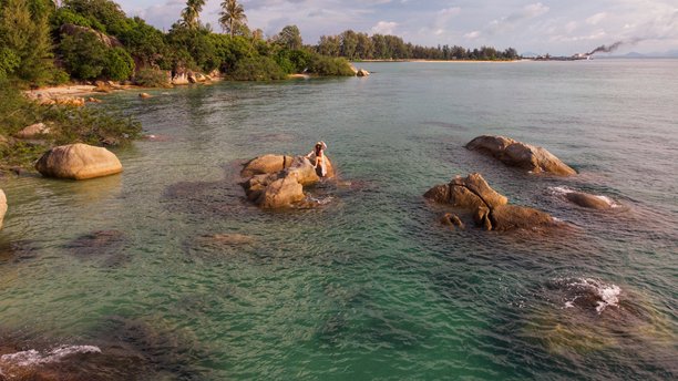 泰国苏梅岛热带岩石海岸上，戴着面纱和太阳帽的年轻女孩摆姿势，航拍照片图片下载