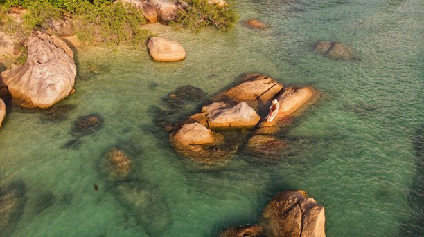 泰国苏梅岛热带岩石海岸，戴着面纱和太阳帽的年轻女孩摆姿势，航拍照片图片下载