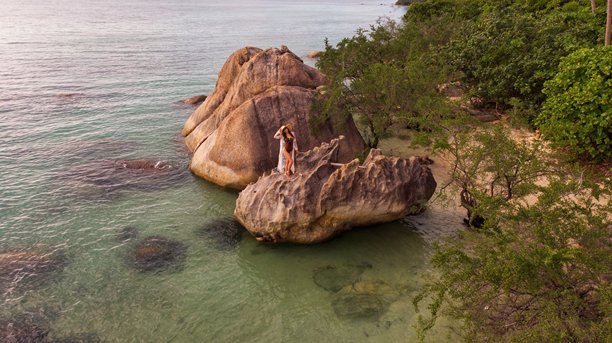 泰国苏梅岛热带岩石海岸，戴着面纱和太阳帽的年轻女孩摆拍，航拍照片图片下载